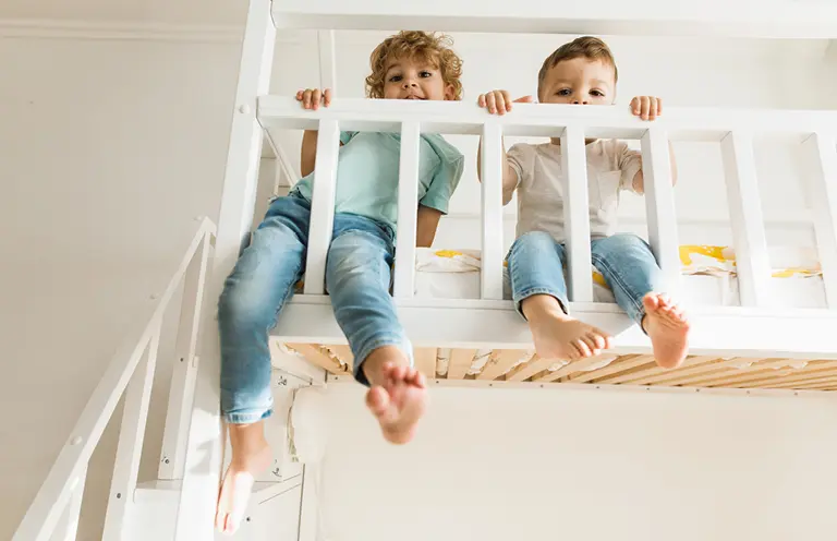 Zwei Jungen spielen auf einem weißen Hochbett im Kinderzimmer – clevere Einrichtung mit Hochbett für kleine Räume schafft zusätzliche Spielfläche und fördert kindgerechtes Wohnen.